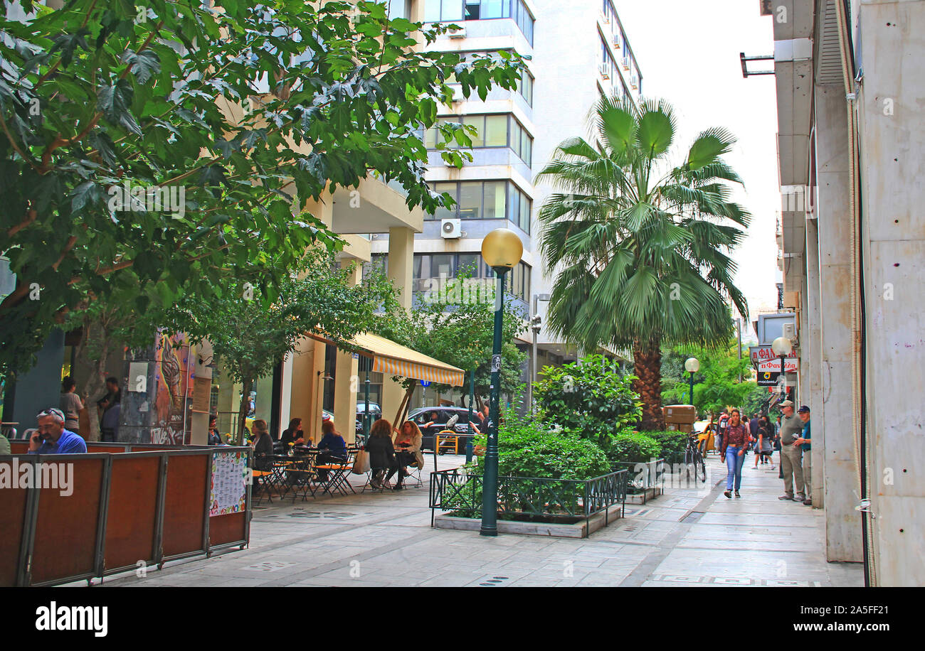 Athen, Attika, Griechenland - 17. Oktober 2018: Touristen wandern und Shopping entlang einer von Bäumen gesäumten Straße in Athen, Griechenland in der Nähe von einem Cafe. Stockfoto
