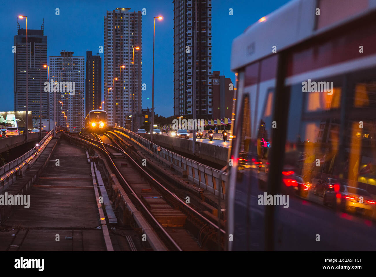 Bangkok, Thailand - 25. Juni 2019: BTS-Zug kommt in Saphan Taksin Station in der Nacht. Hochhäuser der Khlong Ton Sai, Khlong San. Stockfoto