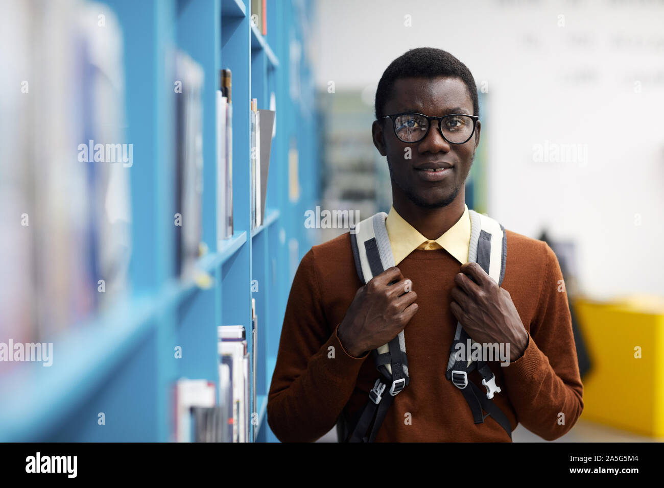 Taille bis Portrait von afroamerikanischen Student an der Kamera schaut beim Stehen durch Regale in der Hochschule, Bibliothek, Raum kopieren Stockfoto
