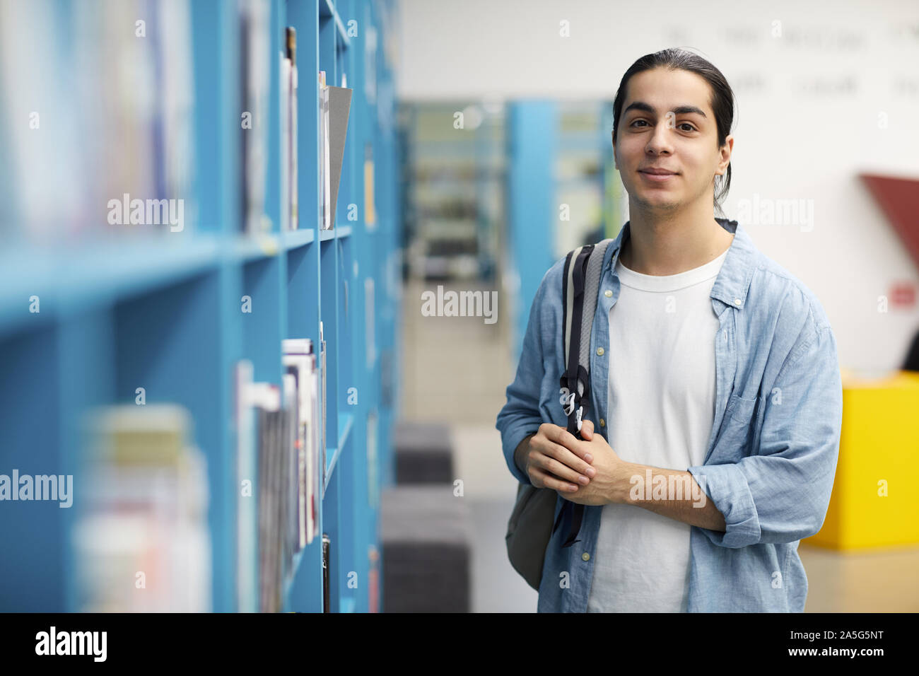 Taille bis Portrait von lateinamerikanischen Student an der Kamera schaut beim Stehen durch Regale in der Hochschule, Bibliothek, Raum kopieren Stockfoto