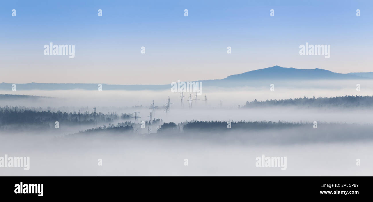 Power Transmission Towers in einem Nebel, in einem bergigen Region im südlichen Jakutien, Russland. Stockfoto