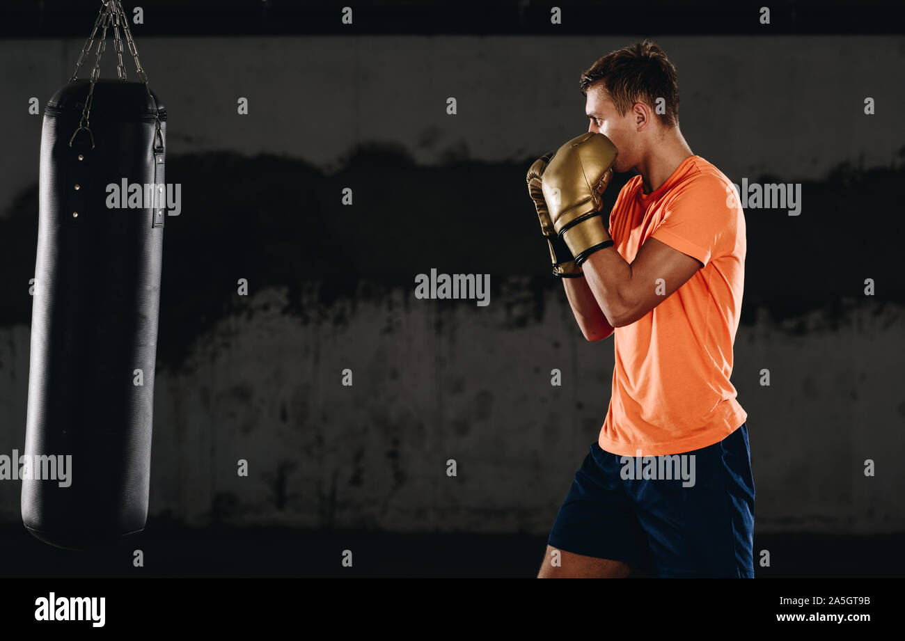 Entschlossene junge Muay Thai Kämpfer Boxhandschuhe Thai Boxing Training mit Boxsack Stockfoto