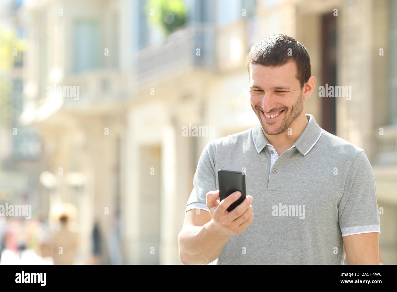 Glückliche erwachsene Mann Kontrolle Handy Inhalt zu Fuß auf der Straße Stockfoto