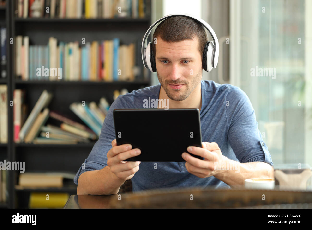 Ernster Mann mit Tablet und Kopfhörer an Online Medien in einem Café sitzend beobachten Stockfoto