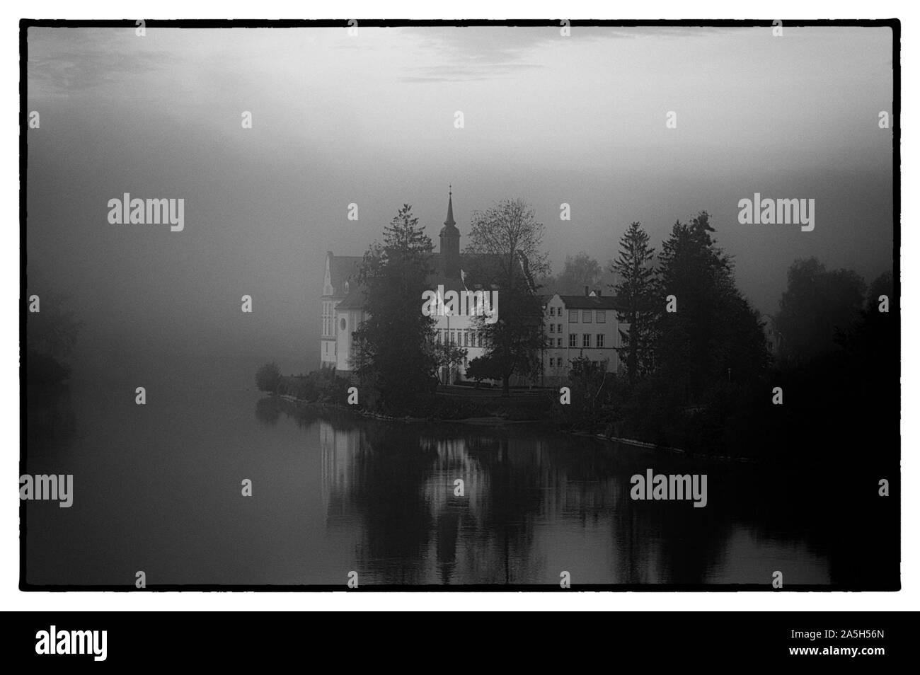 Alte Schule in Bayern im Herbst an einem nebligen Tag am Fluss Schwarz und Weiß Stockfoto