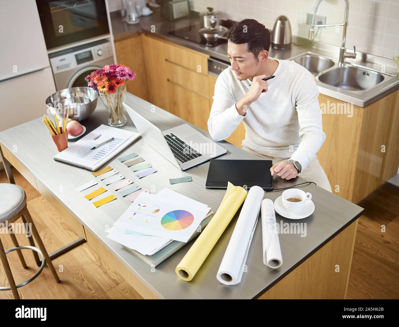 Hohe Betrachtungswinkel und einer jungen asiatischen Designer bei der Arbeitsplatte in der Küche arbeiten an einem mit Laptop Computer und Digital Pen Tablet design Sitzen Stockfoto