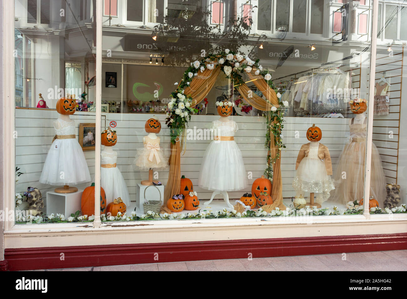 Halloween Kürbisse verwendet als Köpfe auf weißen Kleider in einer kreativen Boutique Shop Fenster anzuzeigen. Stockfoto