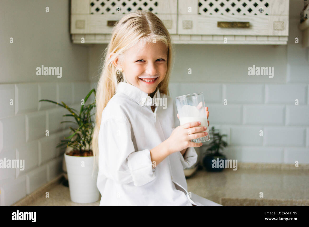 Gerne blonde lange Haare kleines Mädchen trinken Milch in der Küche, gesunder Lebensstil Stockfoto