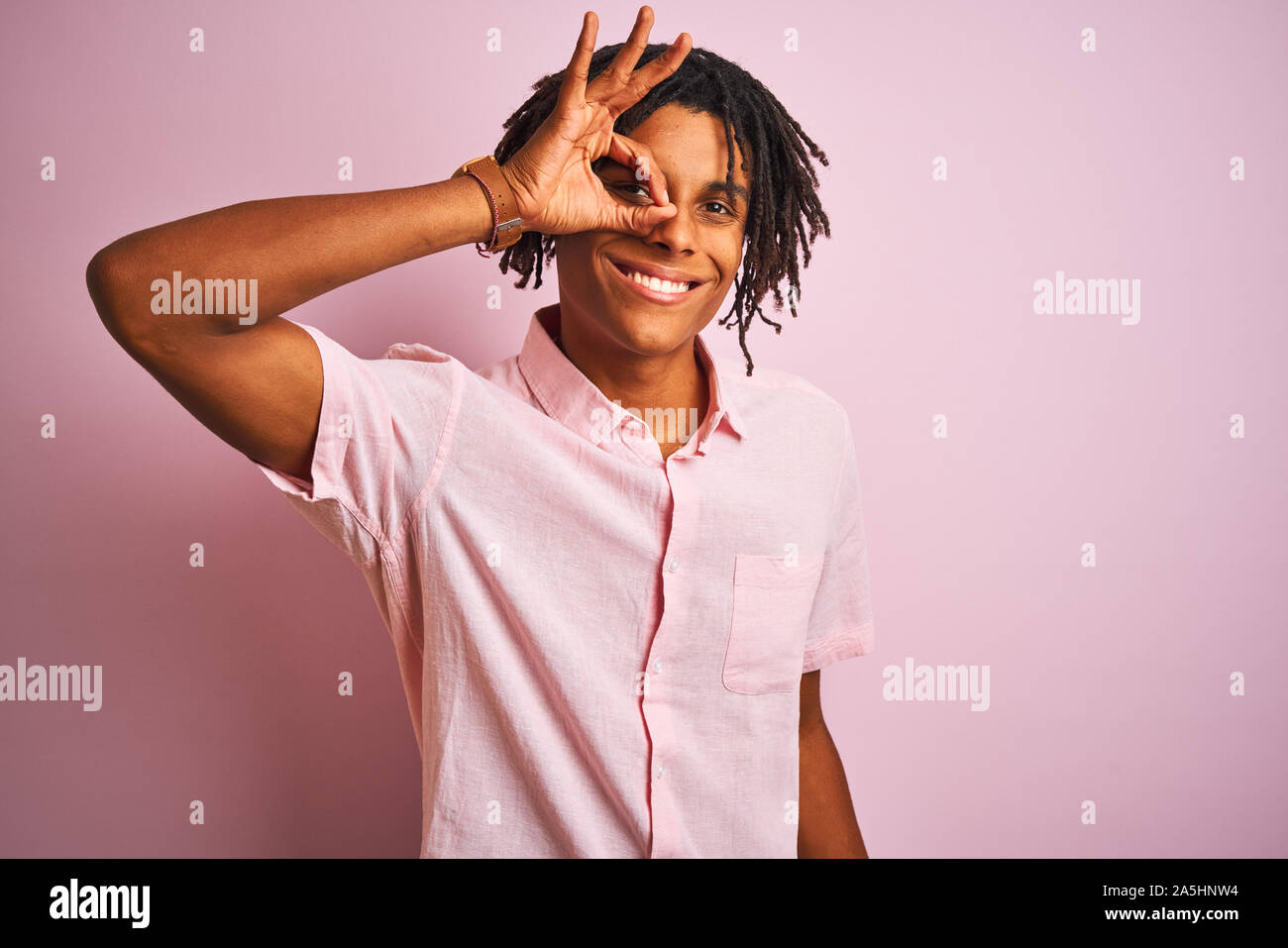 Afro-amerikanische Mann mit Dreadlocks tragen elegante Hemd stehend über isolierte rosa Hintergrund tun ok Geste mit der Hand lächelnd, Auge durch Suchen Stockfoto