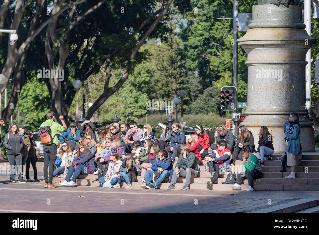 Auf die folgenden Schritte aus, um eine Statue von Queen Victoria in Queens Square, Touristen hören zu einer Guide während einer Tour durch Sydney CBD in Australien Stockfoto