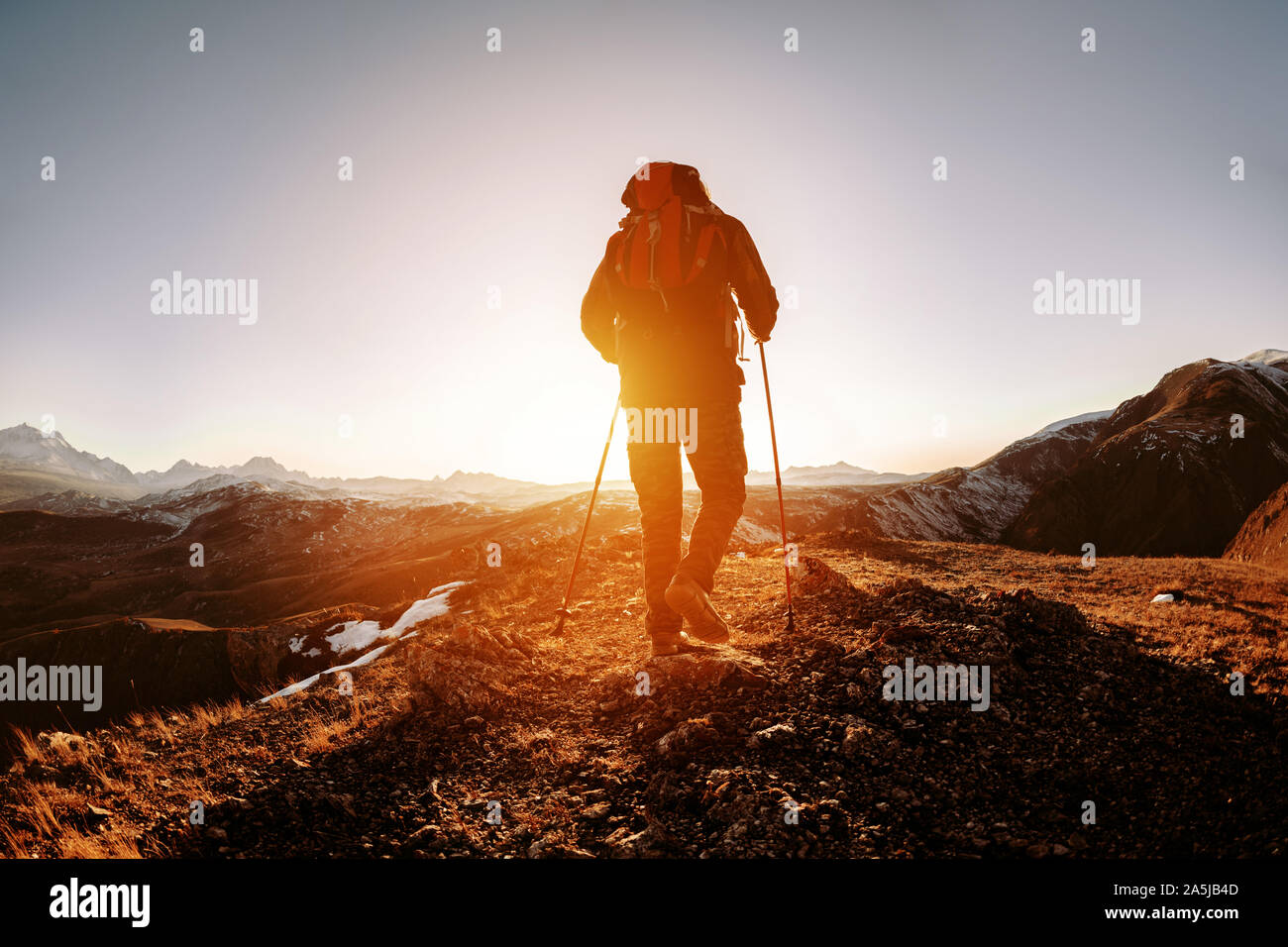 Silhouette der Wanderer mit Rucksack und Wanderstöcke geht in die Berge und den Sonnenuntergang Stockfoto