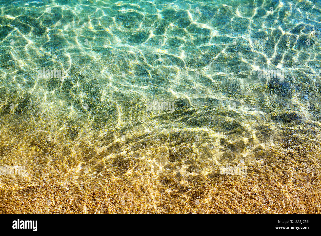 Golden Sand unter klaren, blauen Meer Wasser und Sonnenlicht leuchten Reflexion Nahaufnahme, Ansicht von oben, gelben Sandstrand Textur unter transparenten Meer Oberfläche Stockfoto