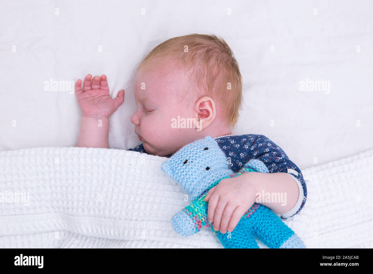 Eine nette junge Baby schlafend unter einer Decke umarmt einen gestrickten Teddybär Stockfoto
