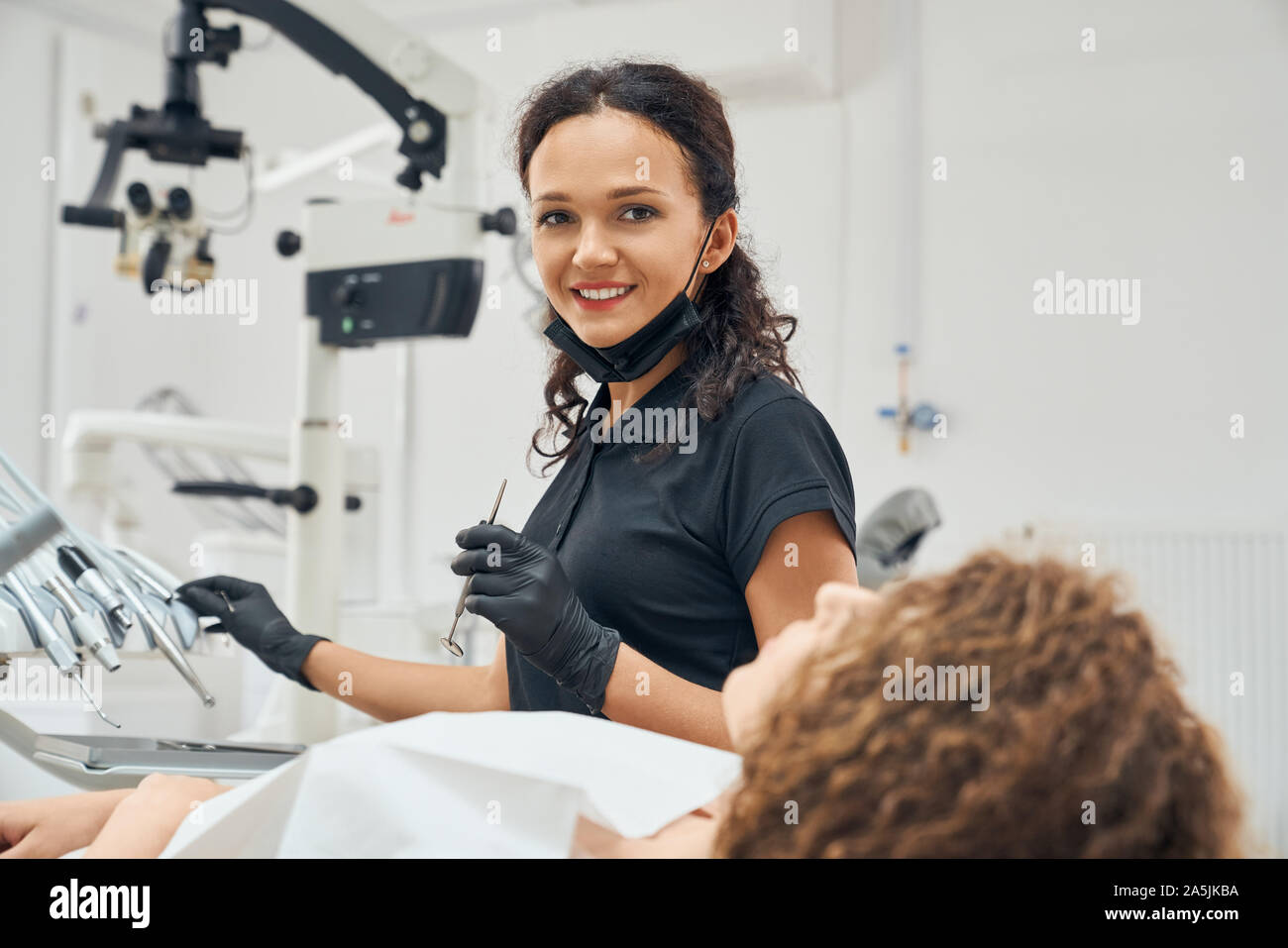 Seitenansicht der glücklichen weiblichen Zahnarzt in Uniform und Schutzhandschuhe an Kamera suchen, lächeln und posieren, während in der zahnmedizinischen Büro arbeiten. Frau halten, professionelle Ausrüstung und Werkzeuge in der Klinik. Stockfoto