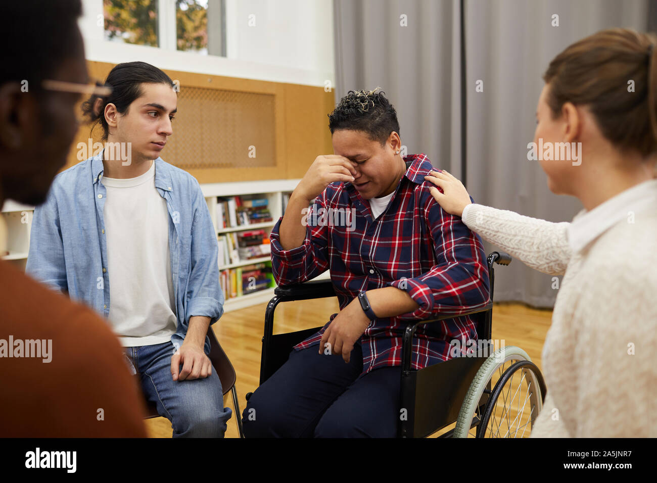 Multi-ethnischen Gruppe von Personen im Kreis sitzend, auf behinderte Frau weinen Sitzen im Rollstuhl während der Sitzung, kopieren Raum konzentrieren Stockfoto