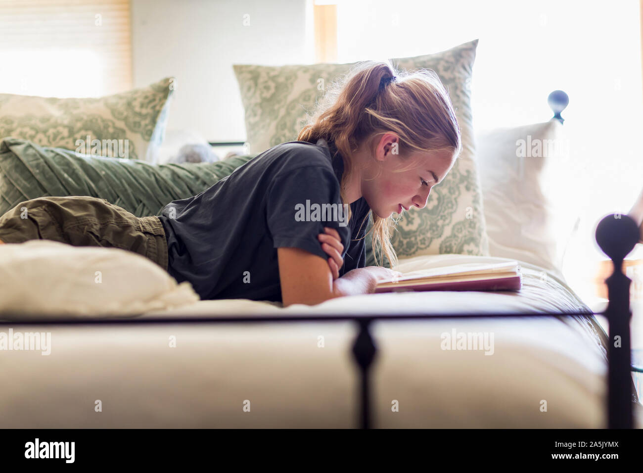 Der 13 Jahre alte Mädchen liegt in ihrem Bett und liest durch Fenster Licht Stockfoto