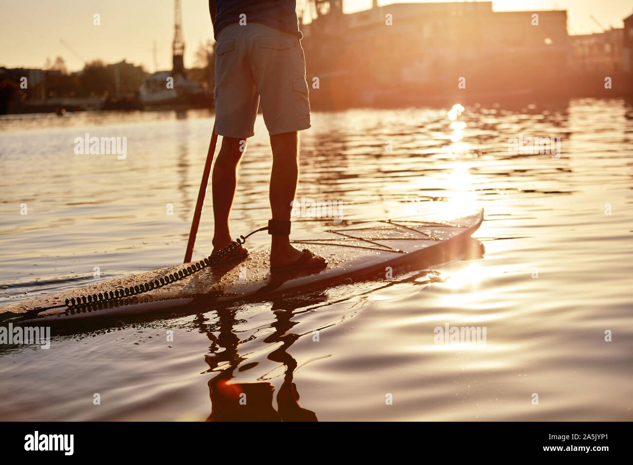 Mann stand auf paddleboard am Fluss in der Dämmerung, Schuß von hinten Stockfoto