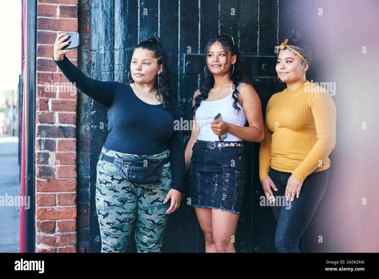 Junge Frau und ihren Schwestern posieren für Smartphone selfie in Gebäude Eingang Stockfoto