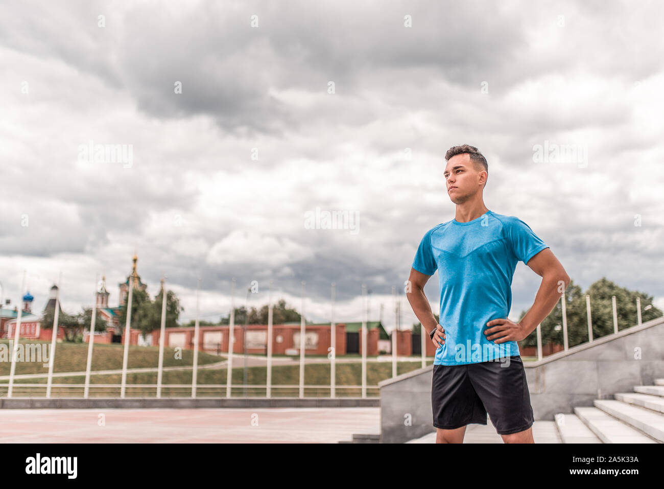 Männliche Athlet blickt zuversichtlich in die Ferne, steuert die Trainer, lehrt Sommer Tag Stadt, Hintergrund cloud. Aktive Jugend Lifestyle, Fitness Workout Stockfoto