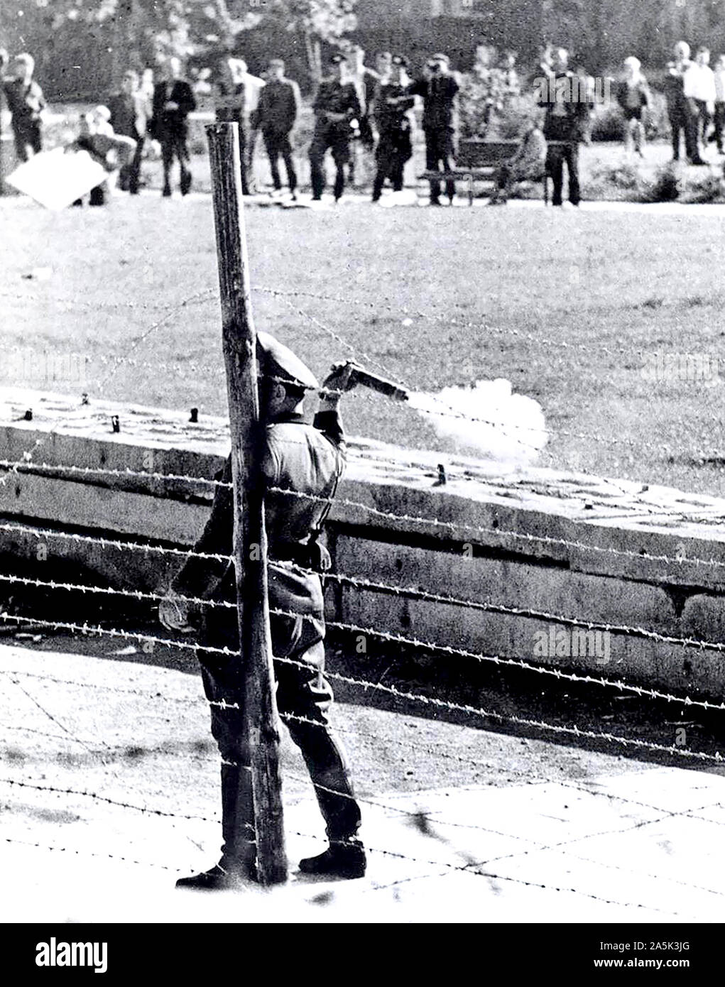 Oktober 1961-kommunistischen "Polizisten" (volkspolizist), stehen zwischen den Grenzzaun und Wand, bereitet eine Tear-Gas Granate bei einer Gruppe von West-berliner, die auf Ihrer Seite der Grenze versammelt die Roten Garden zu Jeer zu werfen Stockfoto