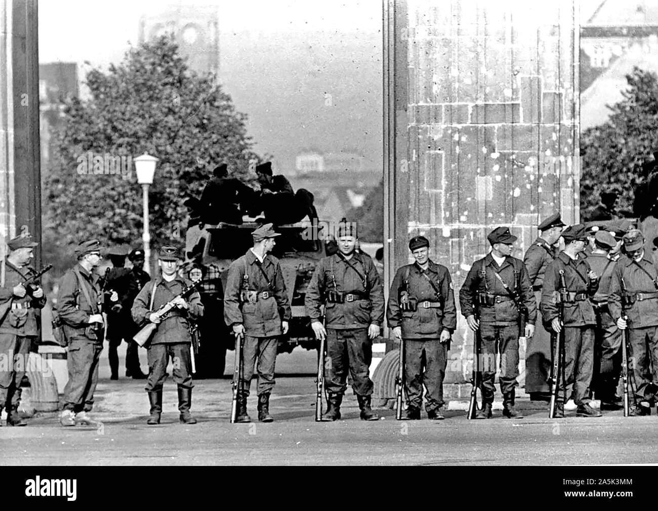 August 1961 - einer Gruppe von Ostberliner "Arbeitermiliz" mit Maschinenpistolen steht Shoulder-To - Schulter vor dem Brandenburger Tor. Hinter Ihnen, die Blockierung der Durchgang, ist eine kommunistische gepanzerten Auto Stockfoto