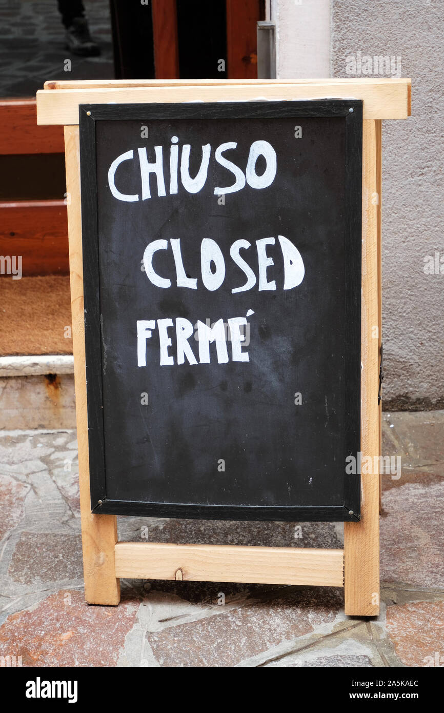 "Chiuso', 'Geschlossen', 'ferme' Zeichen auf schwarzem Brett in drei Sprachen: Englih, Italienisch und Französisch geschrieben Stockfoto