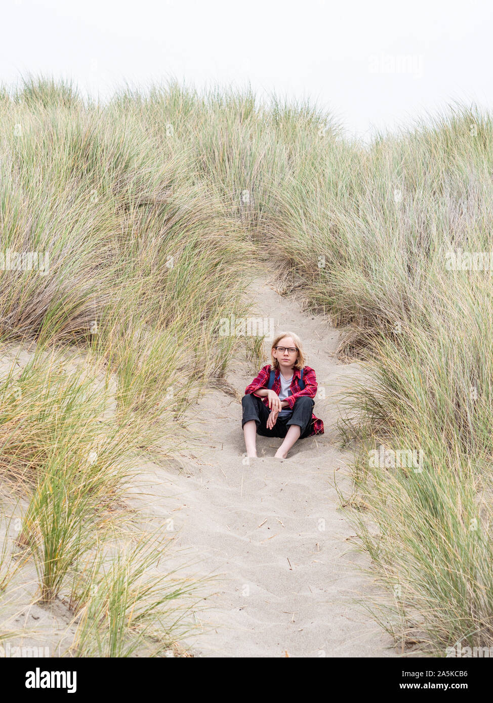 Tween Junge sitzt auf Sand strand Trail im hohen Gras Stockfoto