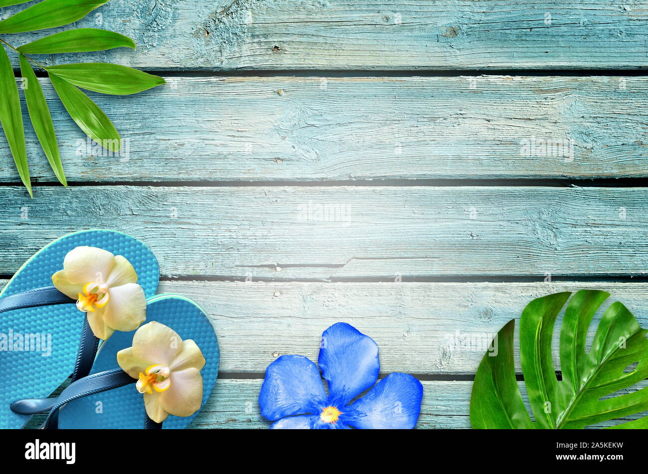 Sommer flachbild Hintergrund legen. Von tropischen Palmen Blätter, Flip Flops und Blume auf alten blauen Holz- Hintergrund. Stockfoto