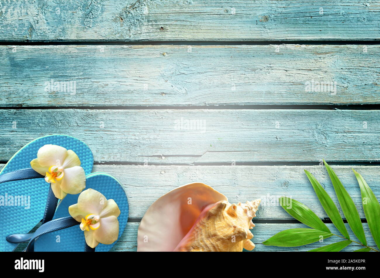 Sommer flachbild Hintergrund legen. Von tropischen Palmen Blätter, Flip Flops und Blume auf alten blauen Holz- Hintergrund. Stockfoto