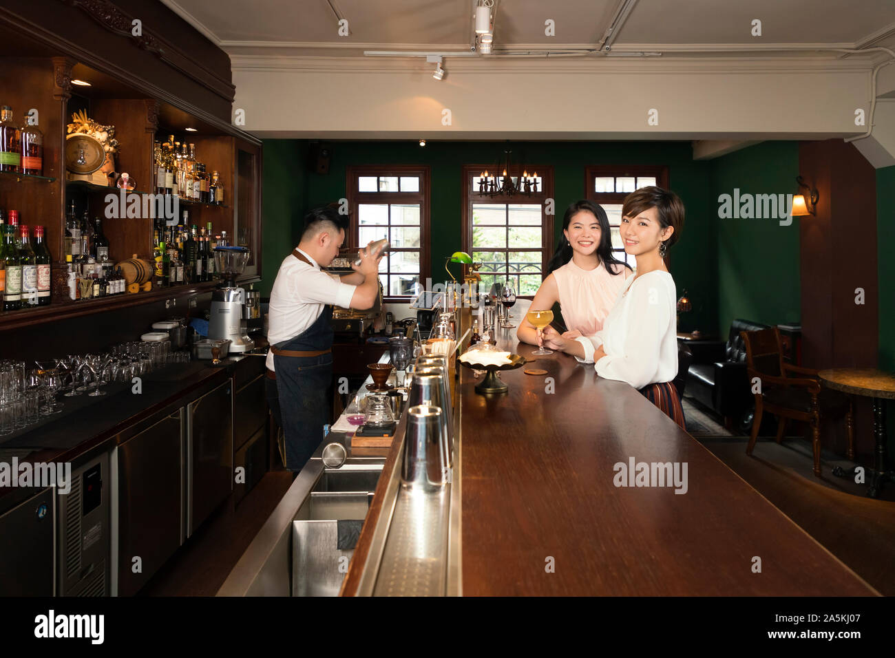 Zwei lächelnde junge Frauen mit Cocktail in der Bar Counter Stockfoto