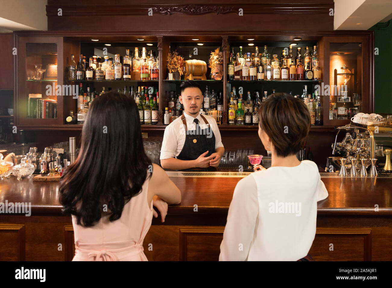 Zwei junge Frauen und Barkeeper an Theke Stockfoto