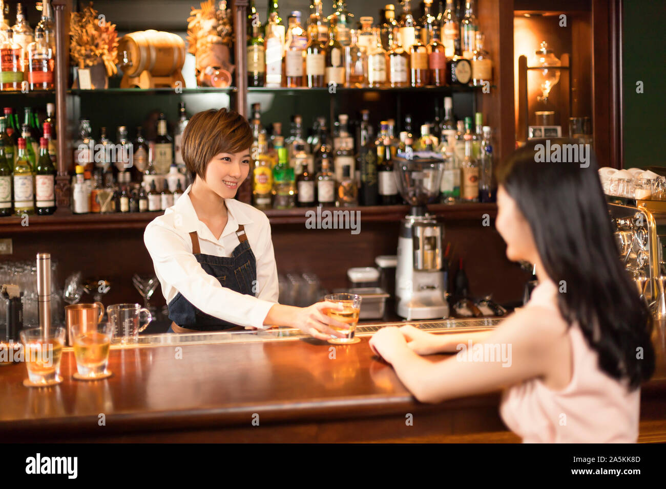 Weiblichen bartender Drink zu Frau an der Theke serviert Stockfoto