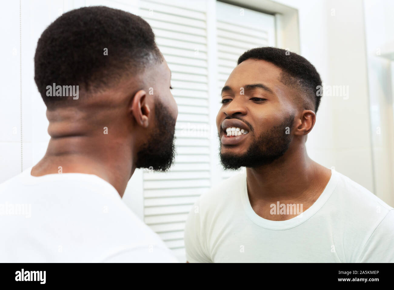 Junge schwarze Mann im Spiegel an seine Zähne in Bad suchen Stockfoto