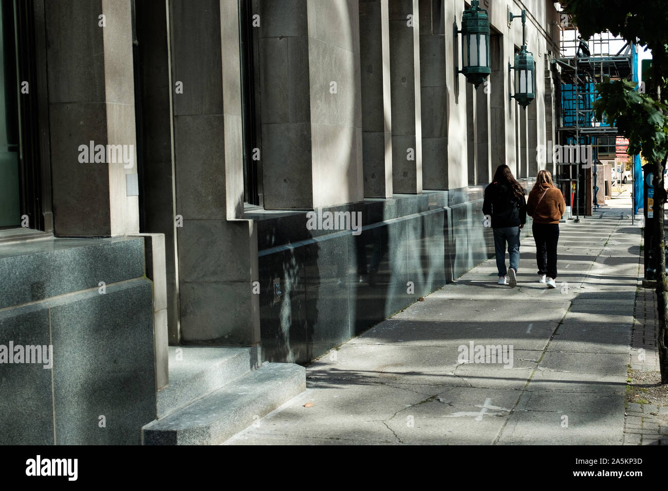 London, Kanada - 18. Oktober 2019. Zwei Frauen gehen Sie eine Straße in reflektierte Sonnenlicht aus den umliegenden Bürogebäuden gebadet. Stockfoto