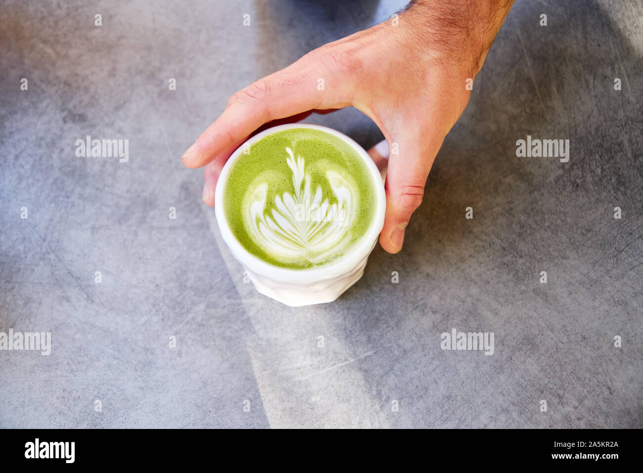 Männliche hand am tisch vegan Matcha Cappuccino mit hafermilch mit latte Kunst im Café im Freien. Stockfoto