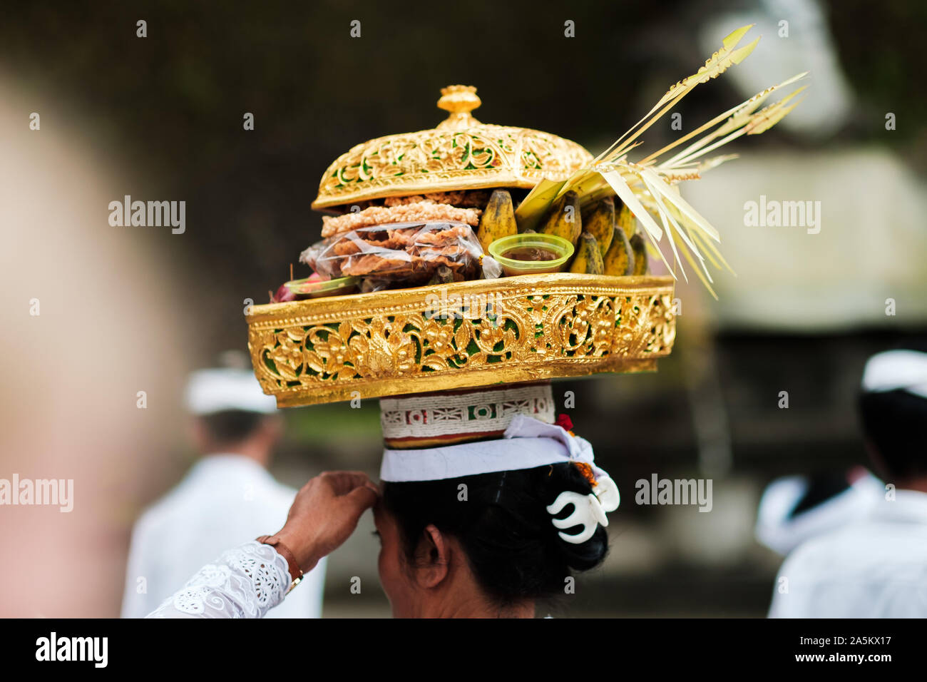 Balinesische Frau in traditionelle festliche Kleidung, die ein Angebot auf Ihren Kopf während der Zeremonie Tage. Die Leute im Hintergrund. Stockfoto