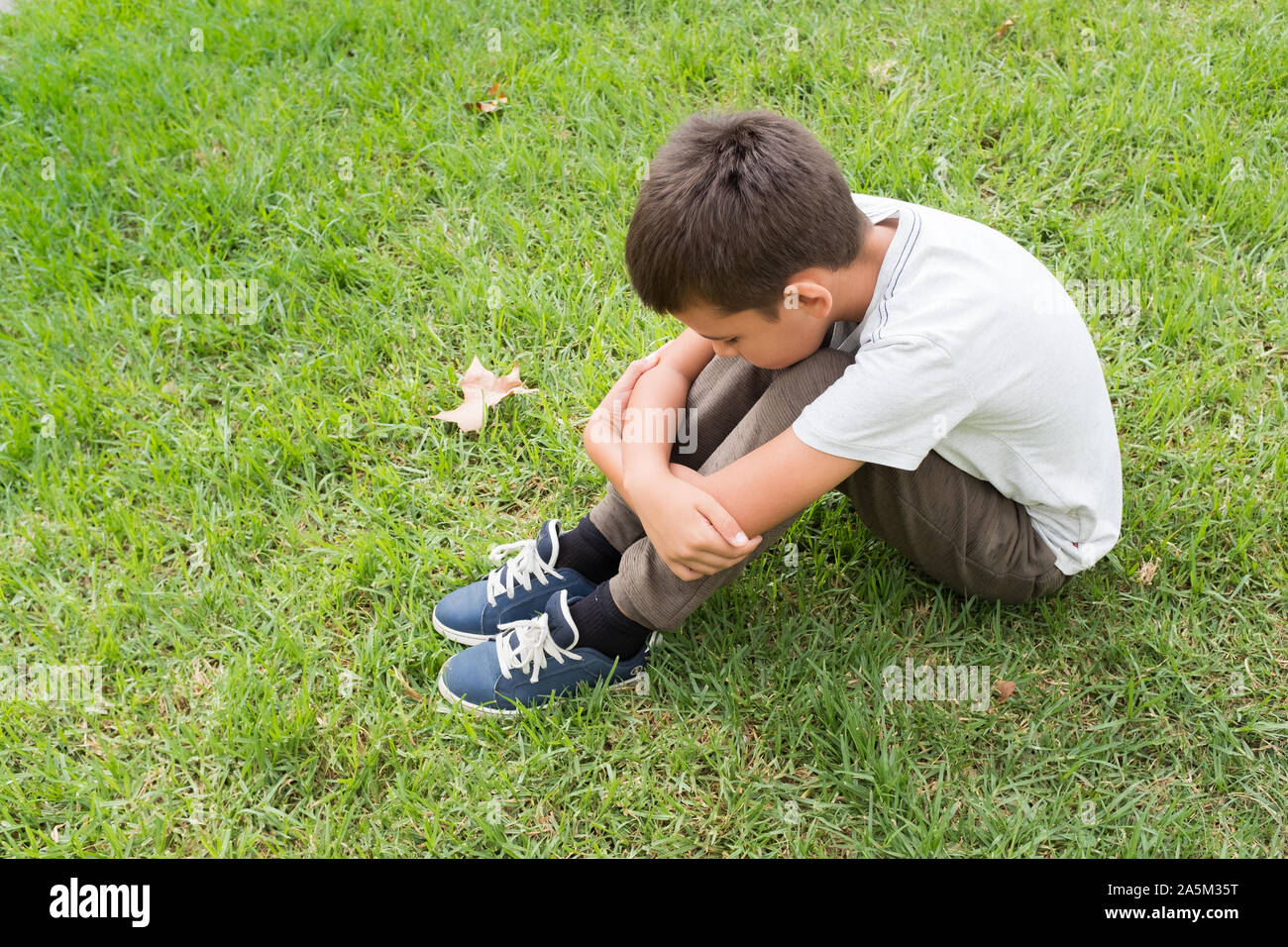 Seitenansicht eines Kindes, das nach unten sitzen auf dem Gras. Verstört, Einsamkeit und Unglück Konzepte. Stockfoto