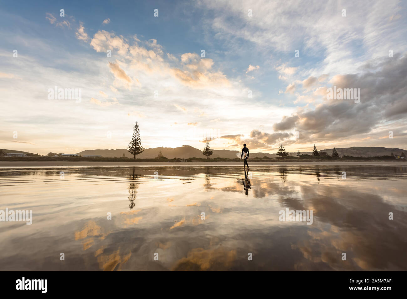 Jugendlich Junge mit Surfbrett zu Fuß am Strand bei Sonnenuntergang Stockfoto