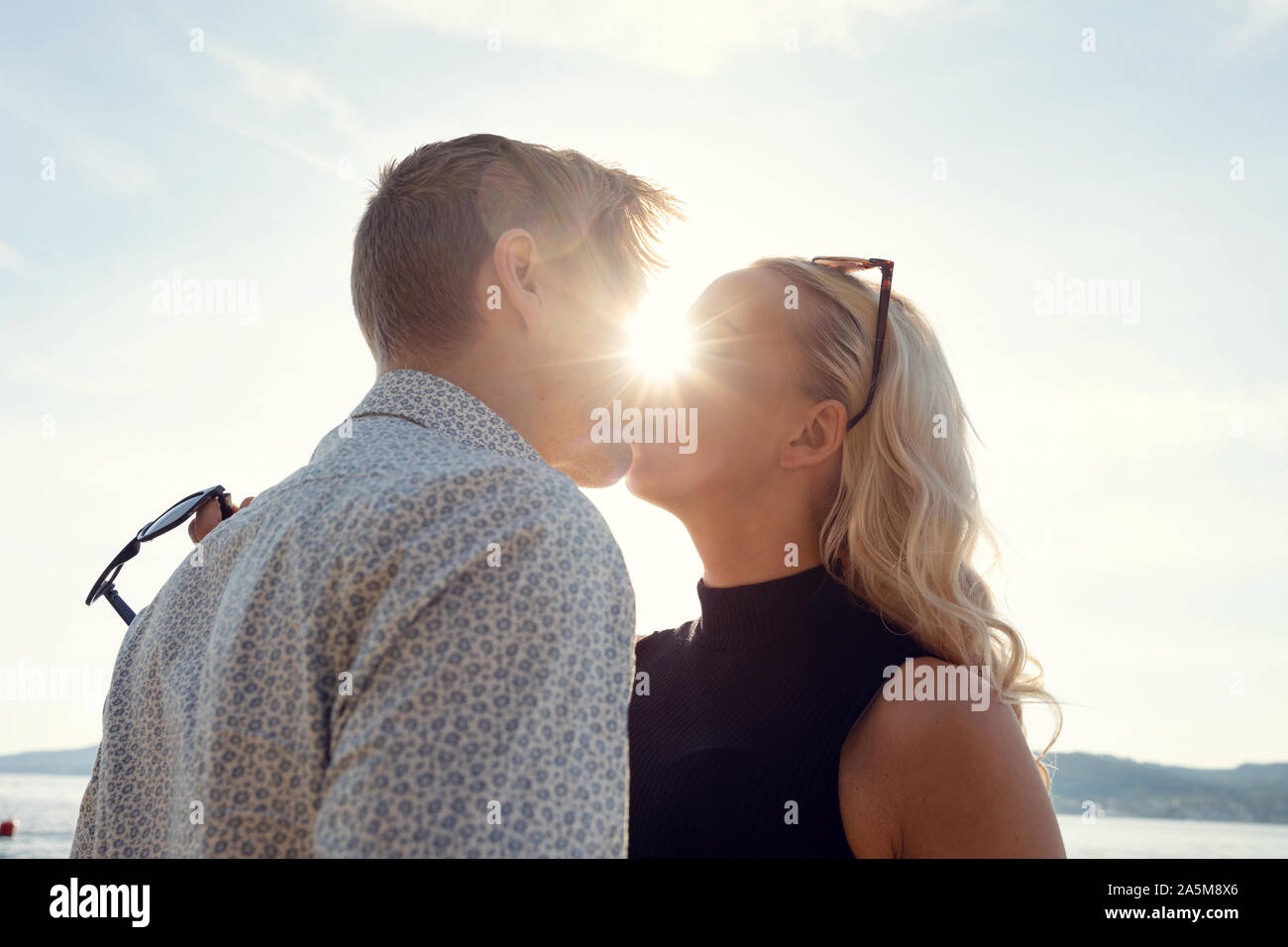 Junges Paar Küssen gegen die Sonne am Strand Stockfoto