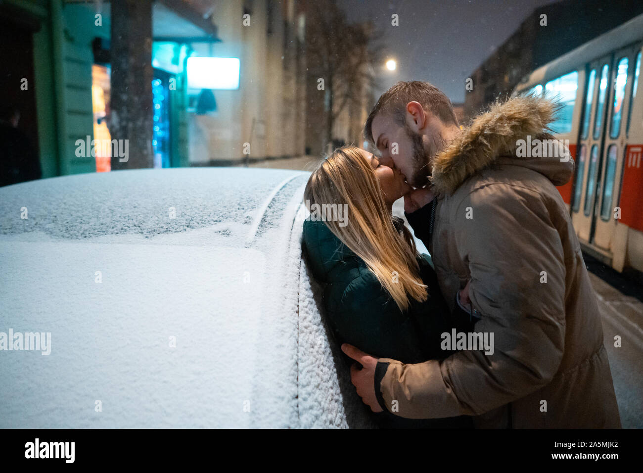 Junge erwachsene Paare küssen einander auf schneebedeckter Straße Stockfoto