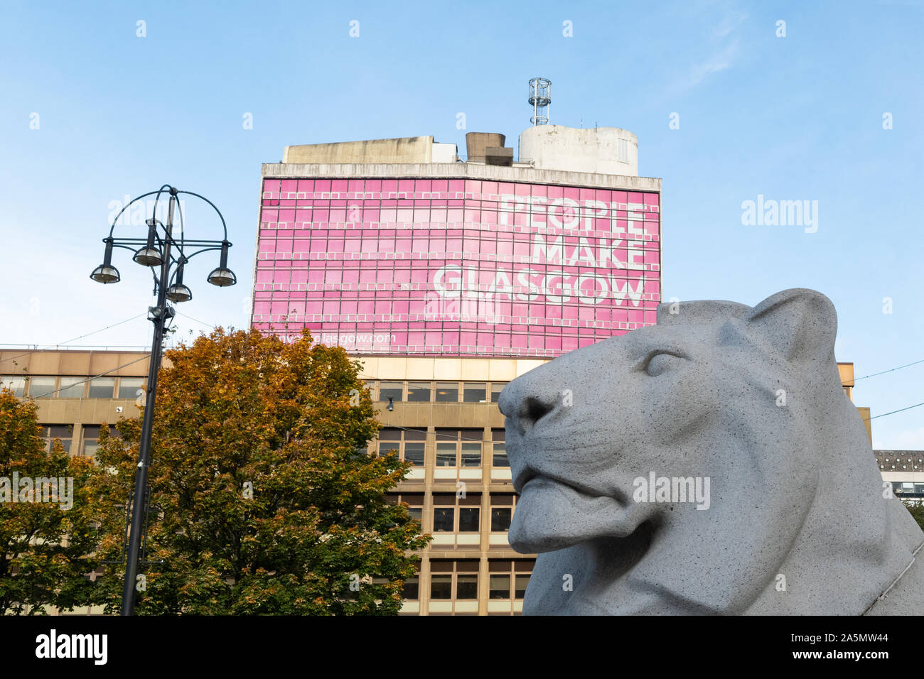 Glasgow George Square - Einer der beiden Löwen Skulpturen neben dem Ehrenmal im Vordergrund und die Leute machen Zeichen hinter Glasgow - Schottland, Großbritannien Stockfoto