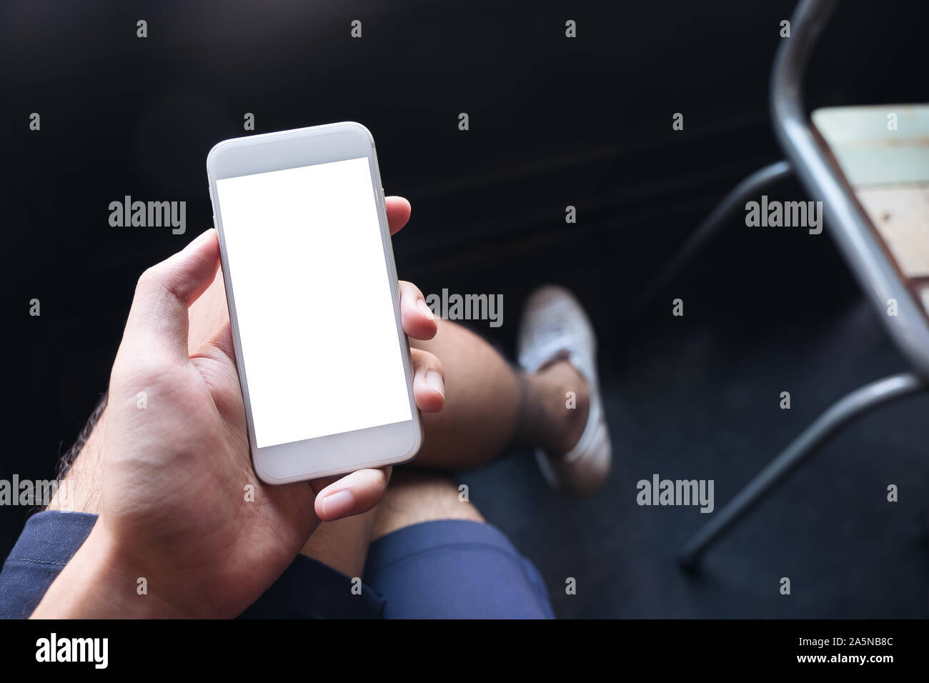 Mockup Bild eines Menschen Hand Holding white Handy mit leeren Desktop Bildschirm auf den Oberschenkel mit weißer Canvas Schuhe in Cafe mit Gefühl entspannt Stockfoto