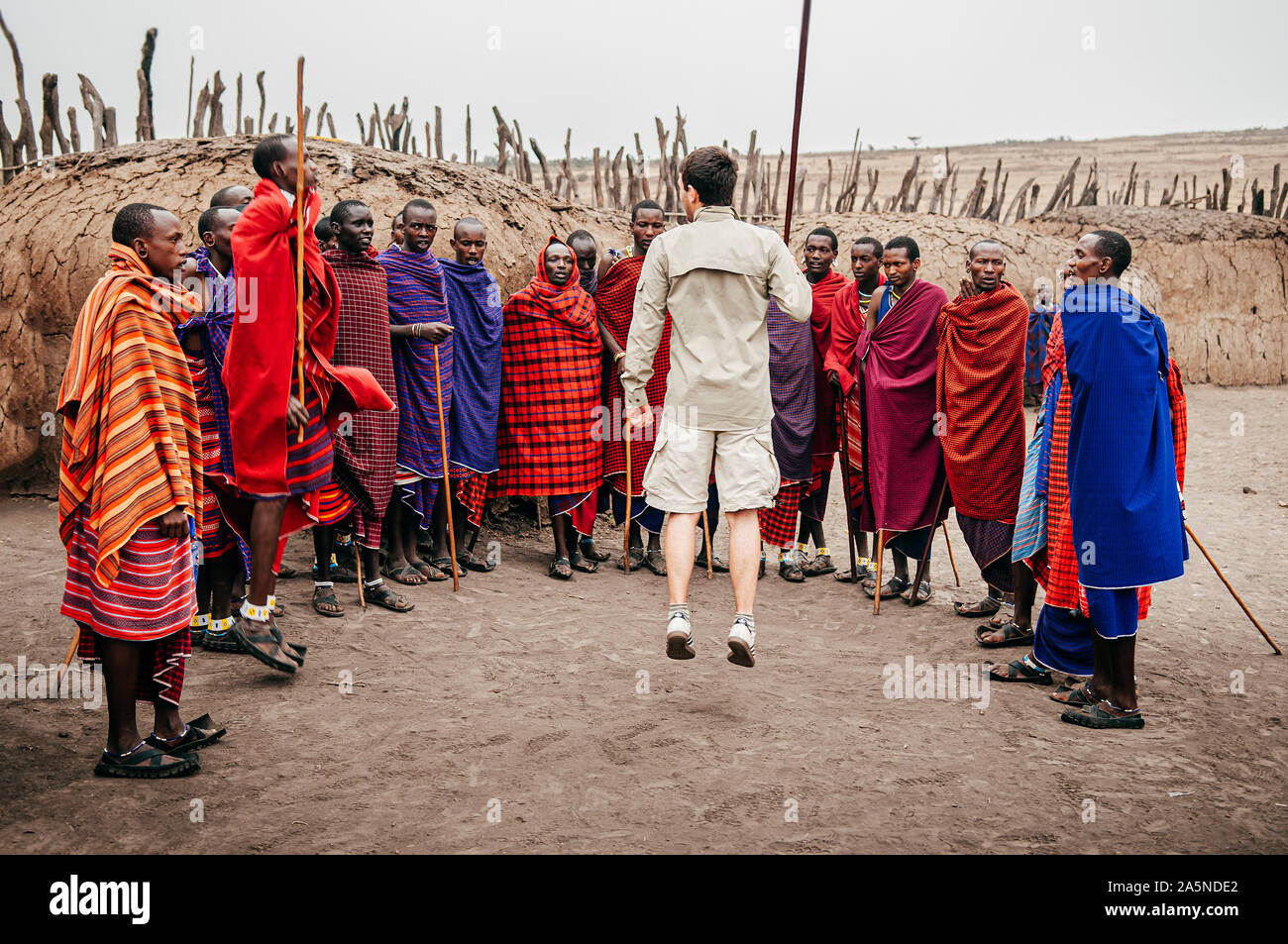 JUN 24, 2011 Serengeti, Tansania - Gruppe der Afrikanischen Masai oder Masai Stamm Mann im roten Tuch stehend von clay Hütte im Dorf und europäischen Touristen jumpin Stockfoto