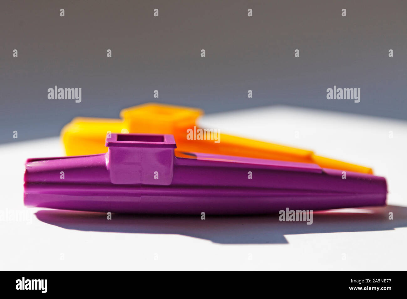 Ein lila und gelb Musikinstrument ist auf einer sonnigen Fensterbank, Kazoo entfernt Stockfoto