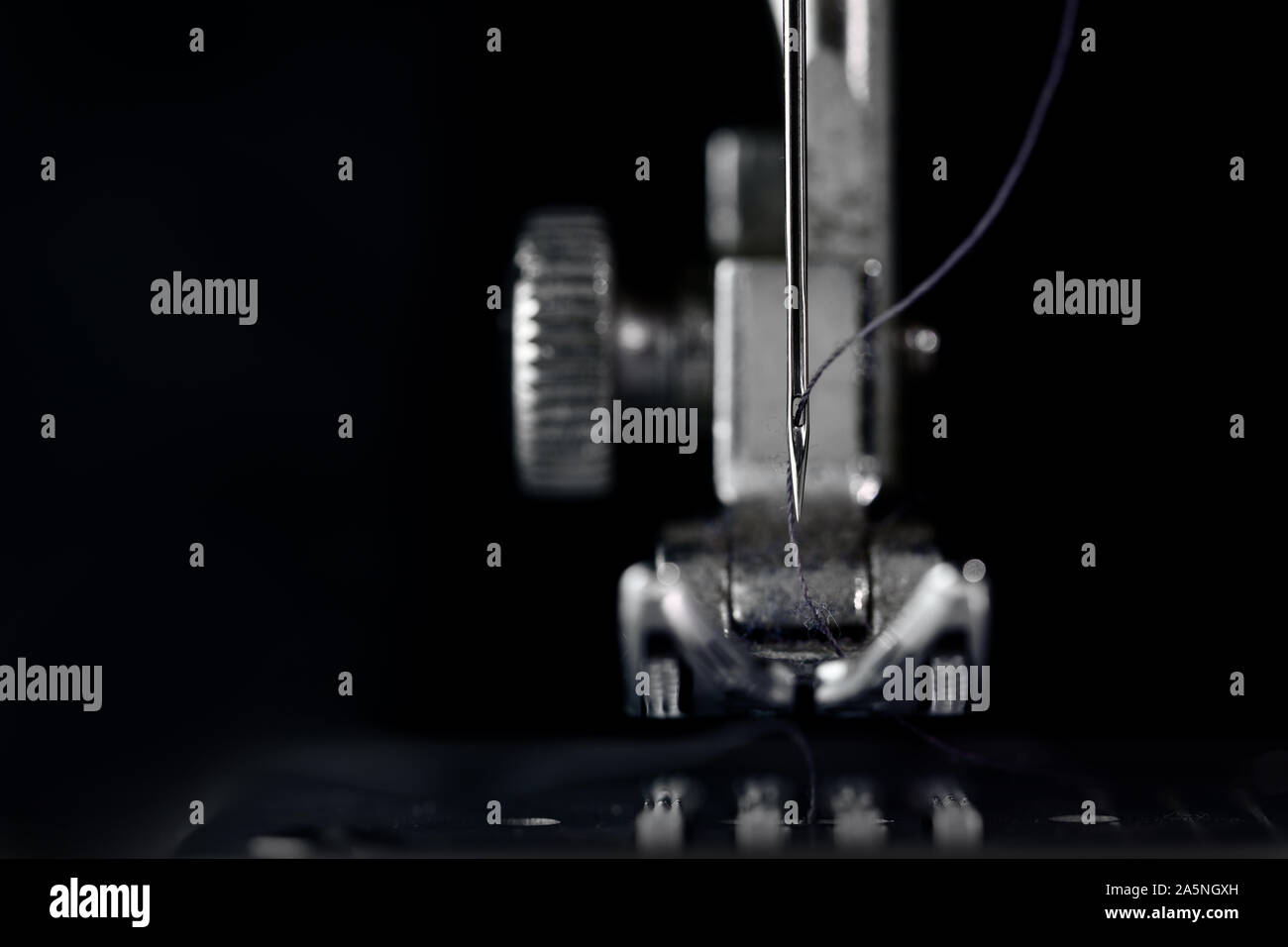 Nadel und nähfuss einer Nähmaschine in der Vorderansicht als extreme Makroaufnahme, technische Erfindung für die Bekleidungsindustrie, dunklen Hintergrund mit c Stockfoto