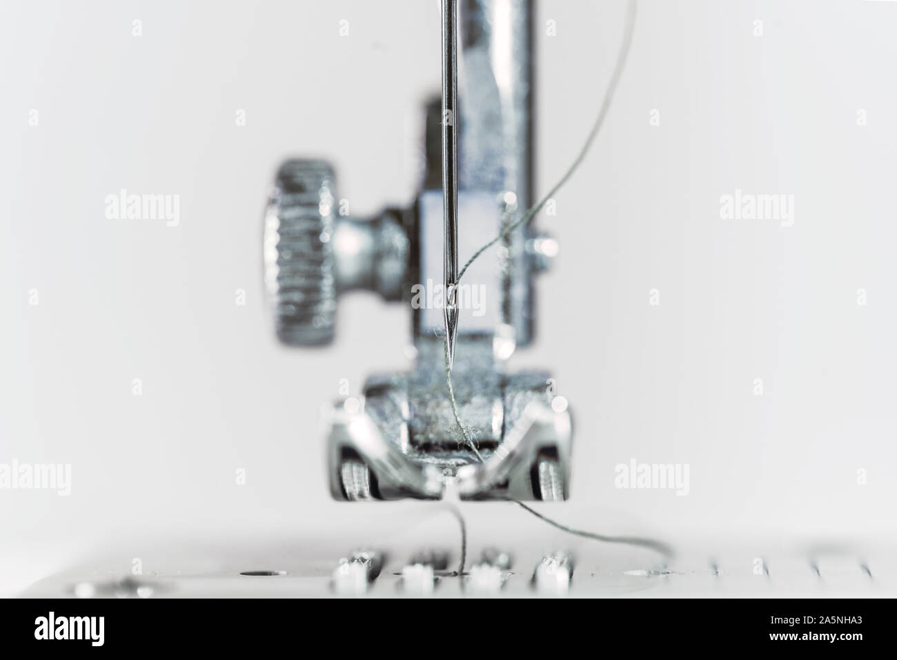 Nadel und nähfuss einer Nähmaschine als extreme Makroaufnahme, technische Erfindung für die Bekleidungsindustrie, heller Hintergrund mit Kopie Raum, s Stockfoto