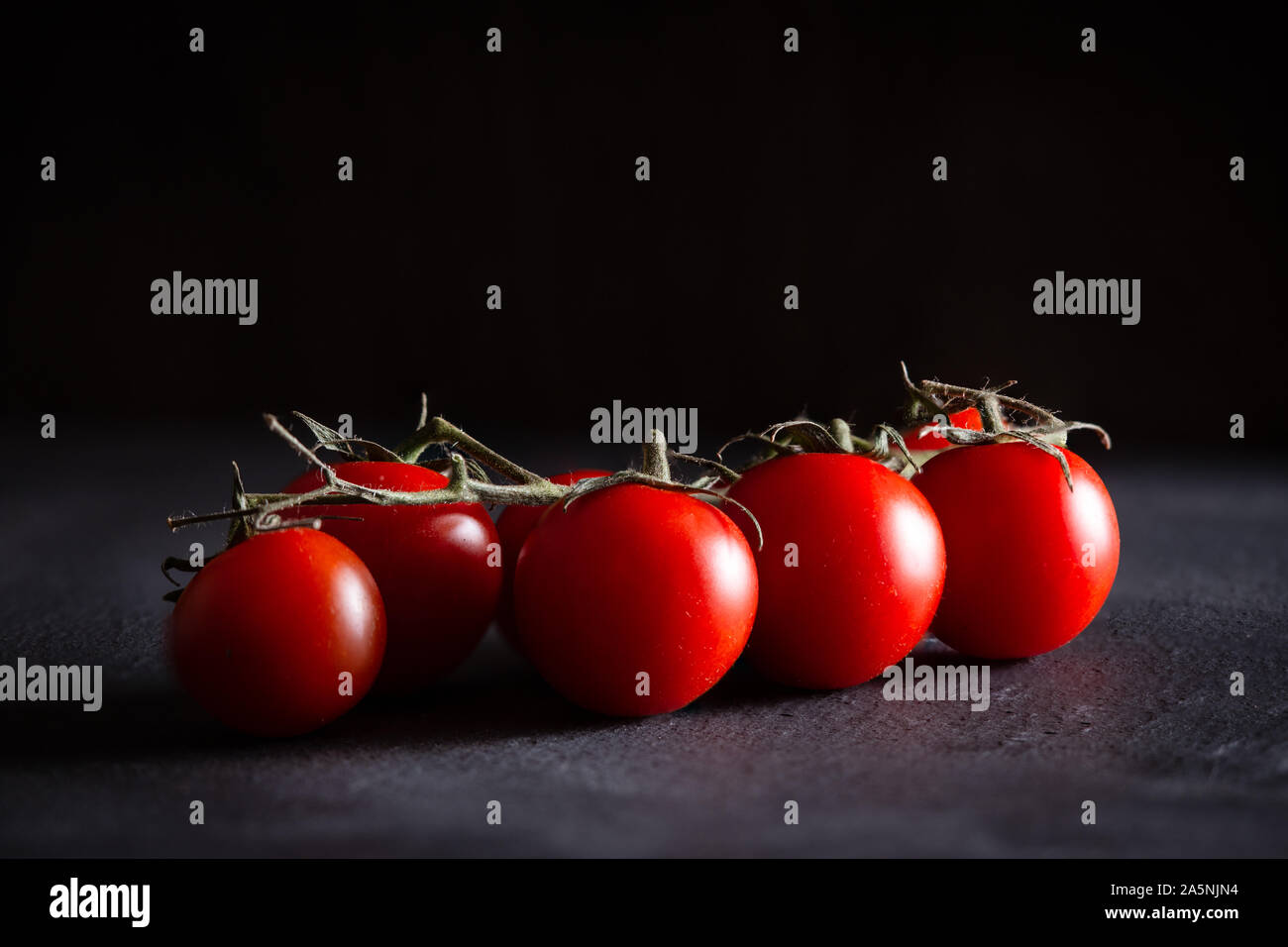 Strauchtomaten auf einem dunkelgrauen Schiefer mit einem schwarzen Hintergrund, Studio erschossen. Vorder- und Hintergrund sind verschwommen mit einem Platz für Text Stockfoto