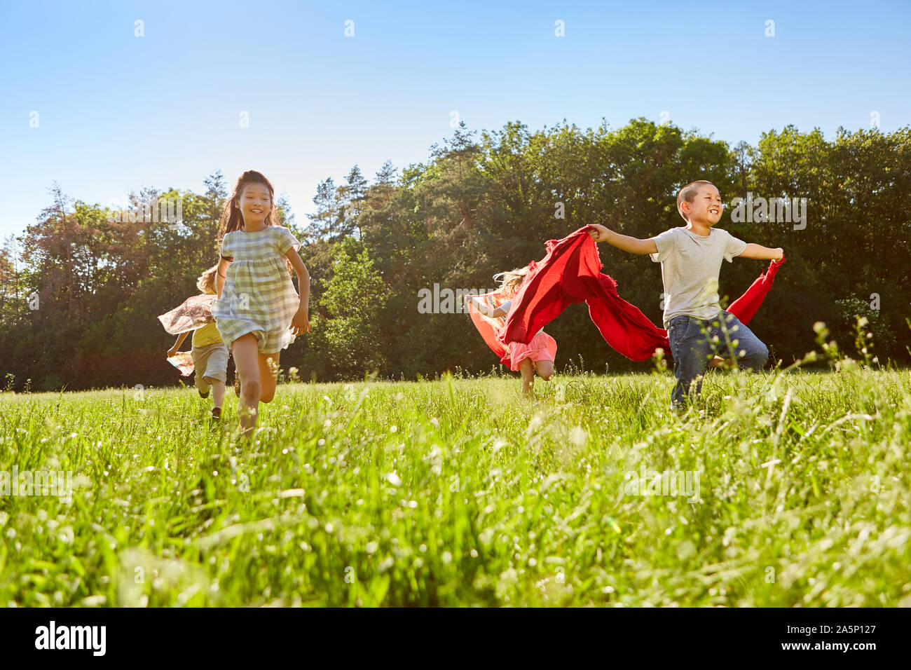 Glückliche Kinder laufen mit Handtüchern über einer Wiese im Sommer Stockfoto
