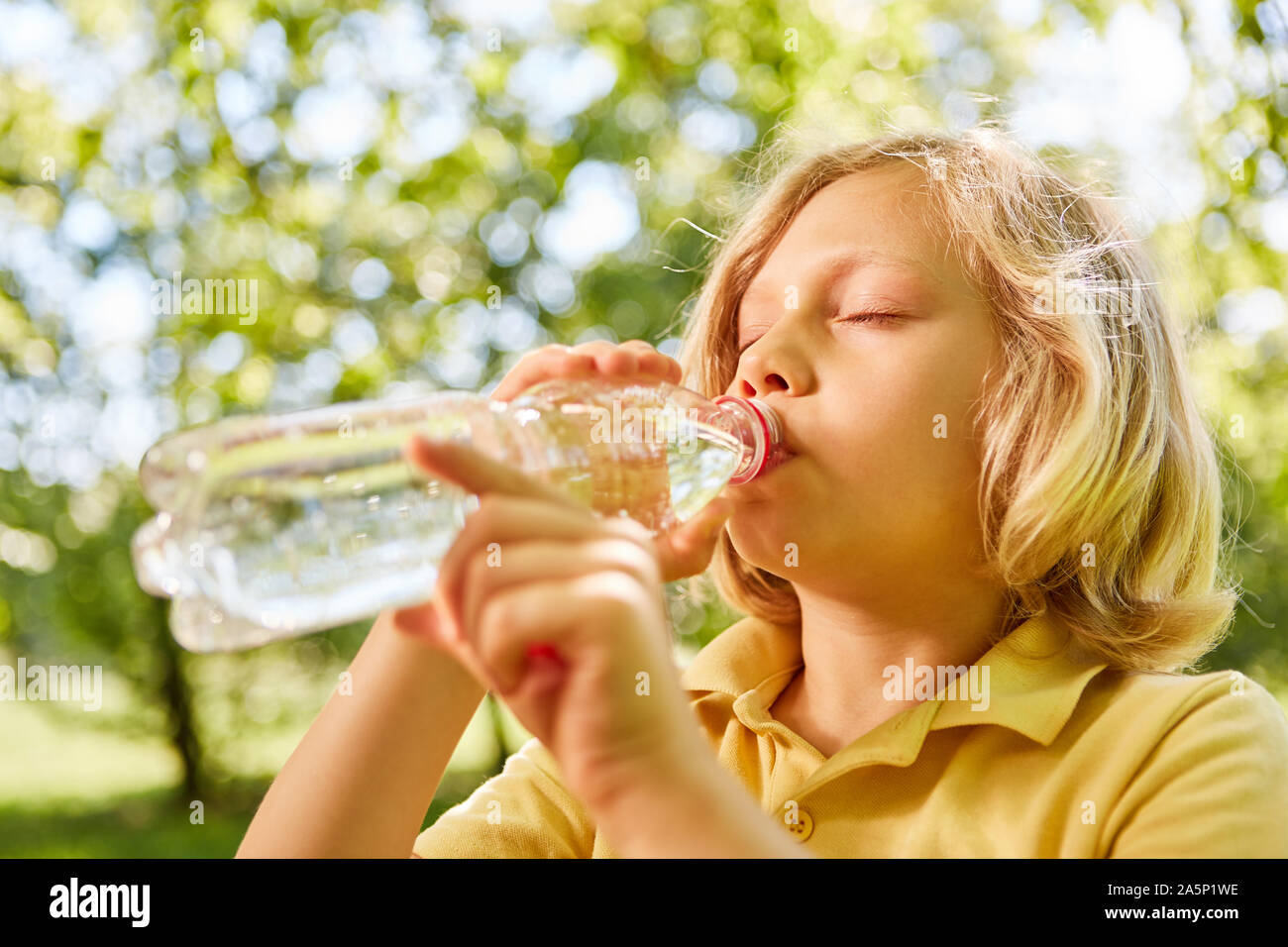 Blonde junge thirstily ist das Trinken aus einer Flasche Mineralwasser im Sommer Stockfoto