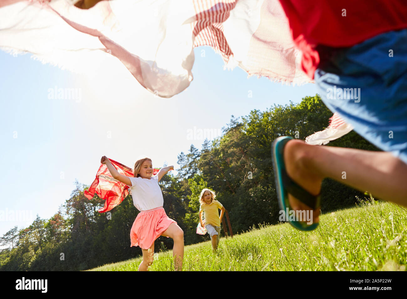 Kinder spielen und laufen mit Handtüchern auf einer Wiese in der Natur Stockfoto